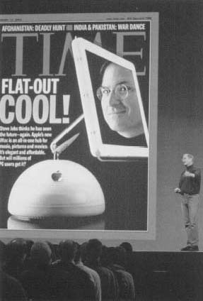 Apple CEO Steve jobs stands next to an enormous cover of Time magazine as he introduces the new flat screen iMac at the Macworld Expo in San Francisco, California, in January 2002. Reproduced by permission of AP/Wide World Photos.