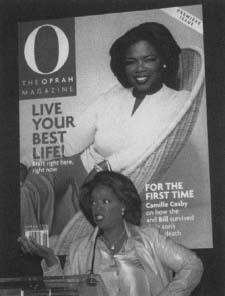Oprah Winfrey standing in front of the cover of the premiere issue of 0, the Oprah Magazine. 0 debuted in April 1999. Reproduced by permission of AP/Wide World Photos.